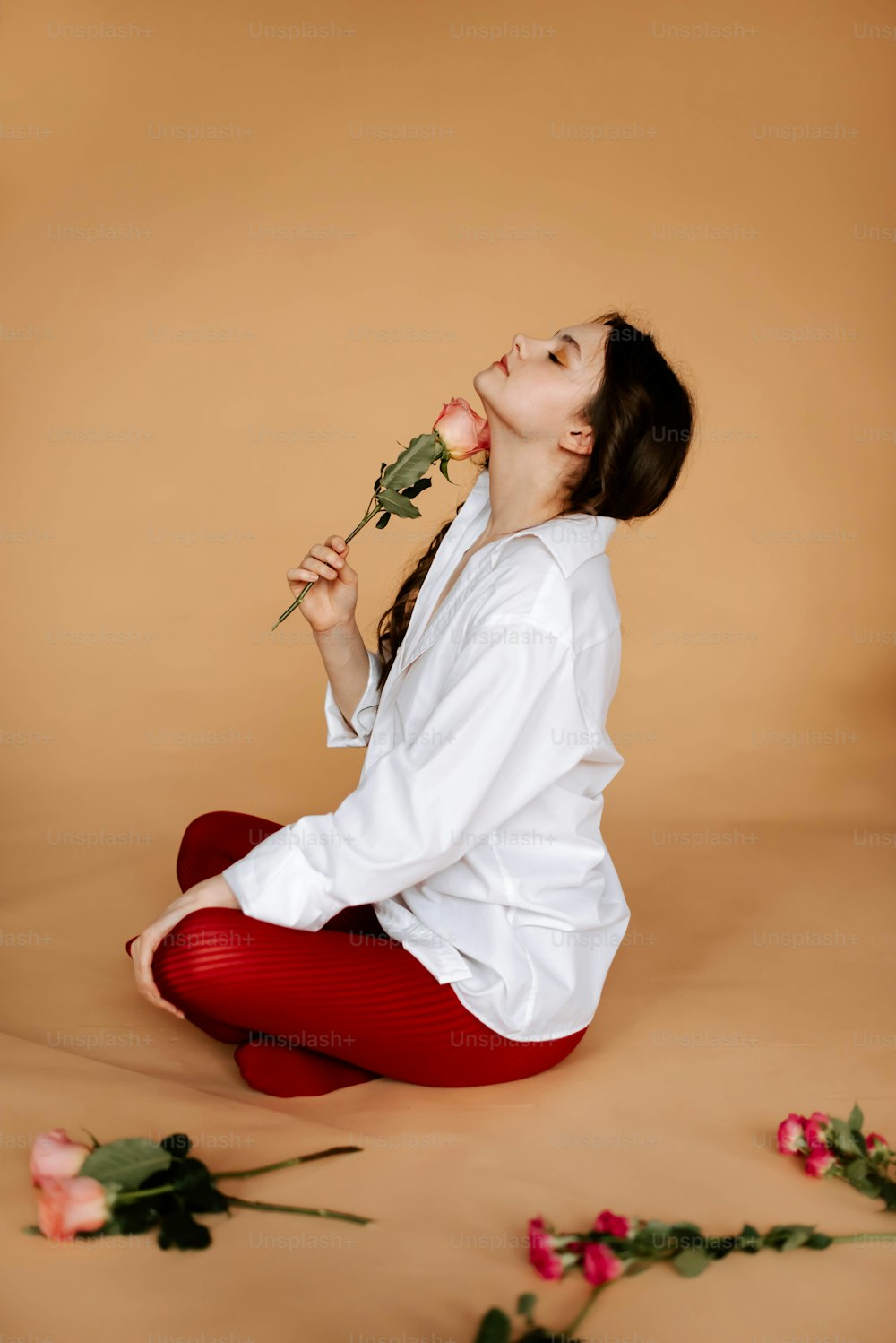 a woman sitting on the ground with a rose in her mouth