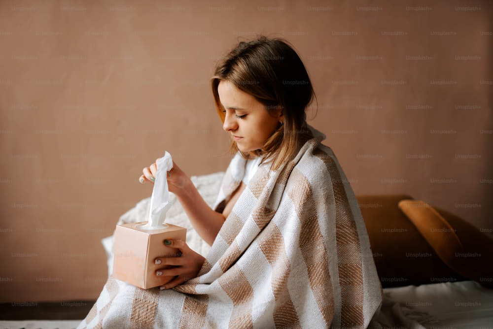 a little girl wrapped in a blanket sitting on a bed