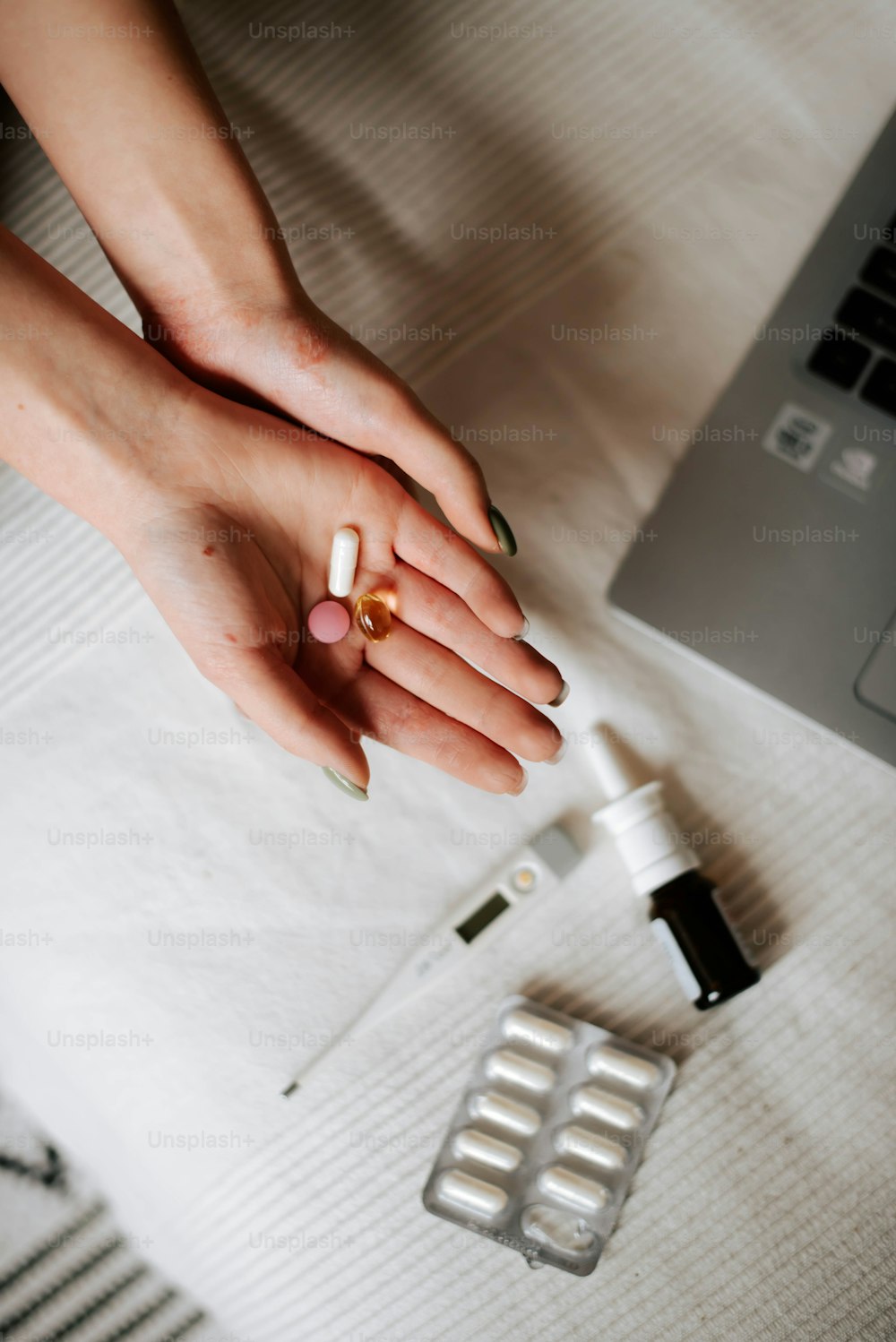 las manos de una mujer sosteniendo un frasco de pastillas y una computadora portátil