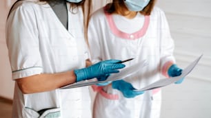 two women in white lab coats and blue gloves