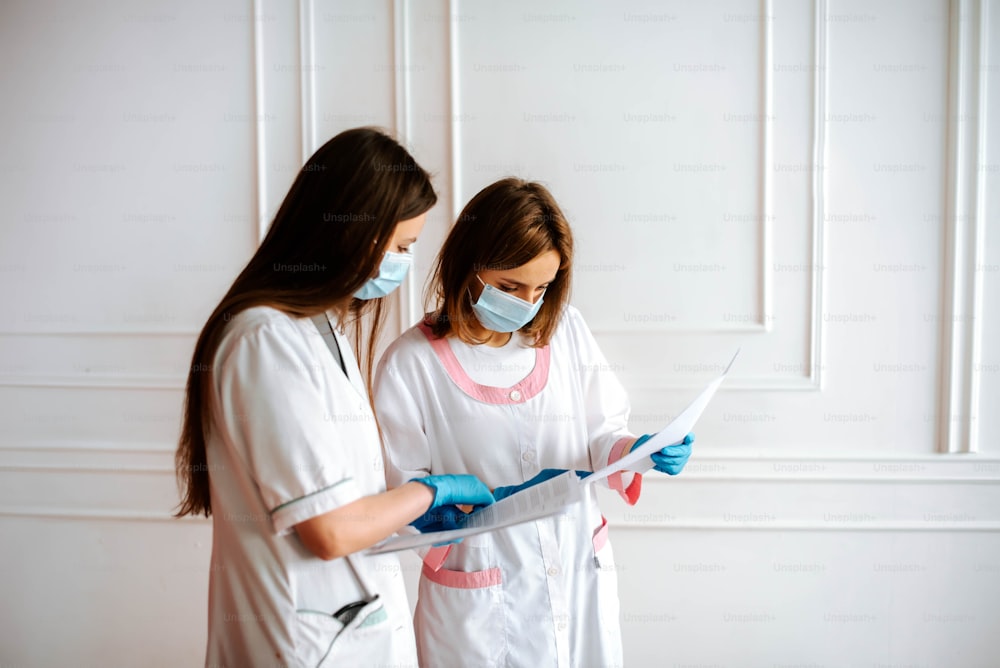 Dos mujeres con batas blancas de laboratorio y máscaras están mirando un pedazo de papel