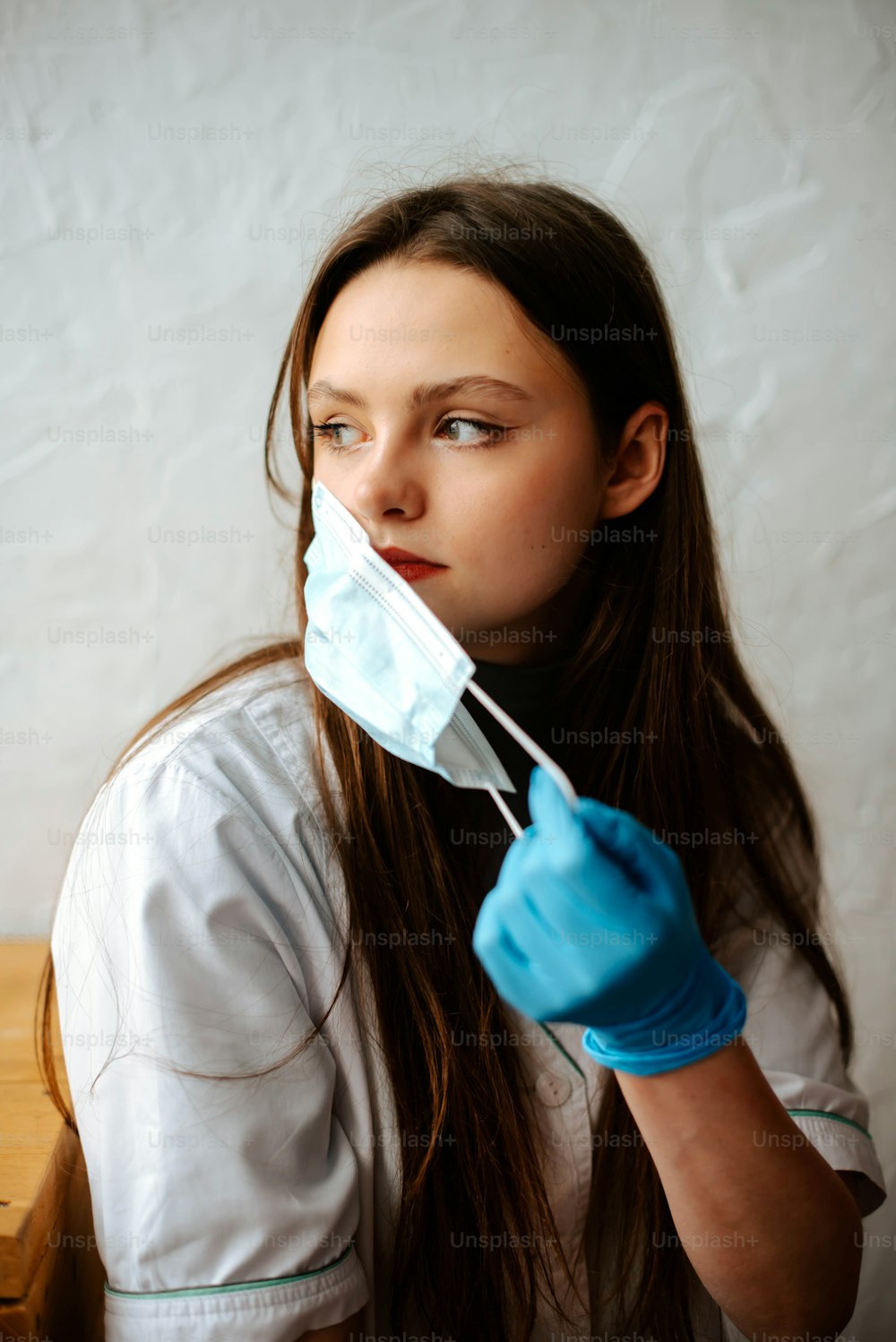 a woman in a white shirt and blue gloves holds a surgical mask over her mouth