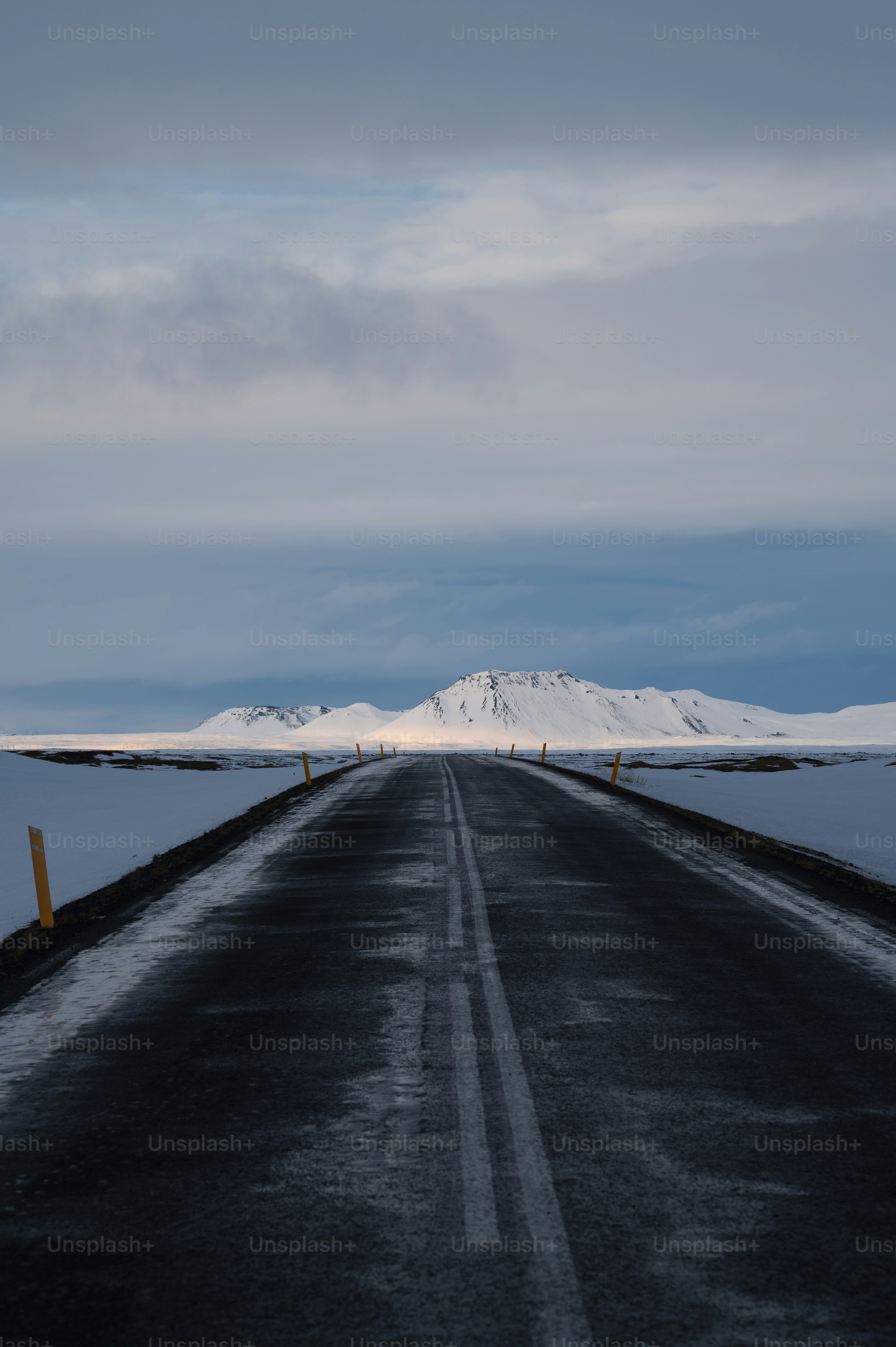 an empty road with snow covered mountains in the background
