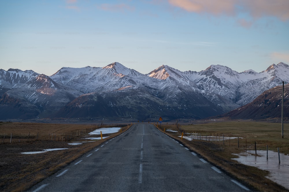 a long road with snow covered mountains in the background
