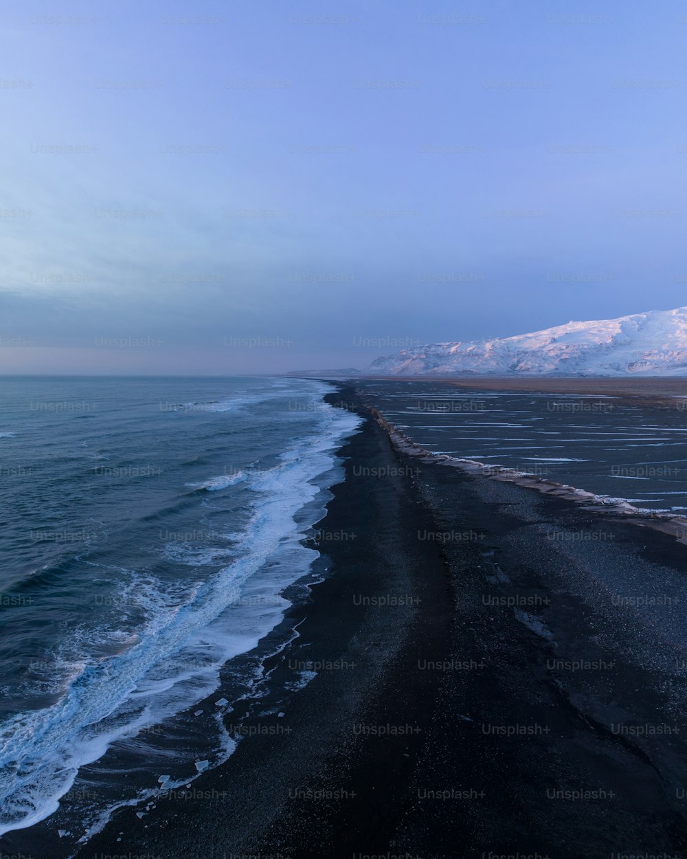 a long stretch of black sand beach next to the ocean