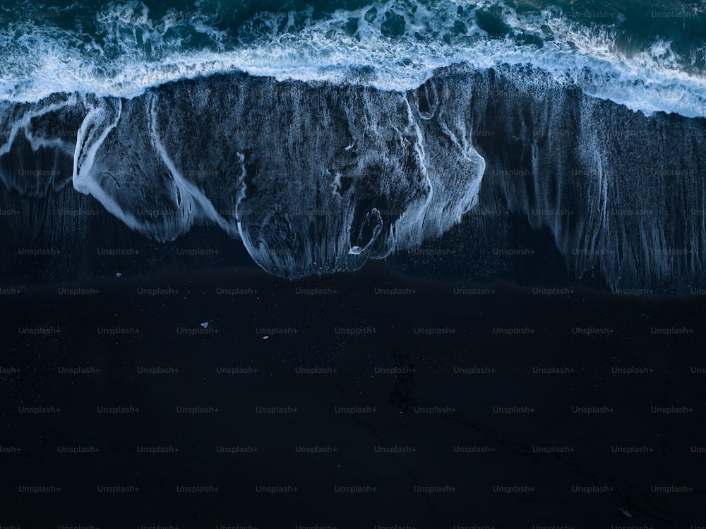 an aerial view of the ocean waves and the black sand beach