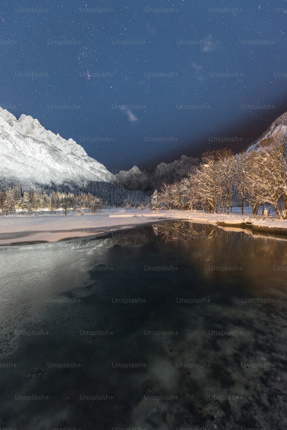 a lake surrounded by snow covered mountains under a night sky