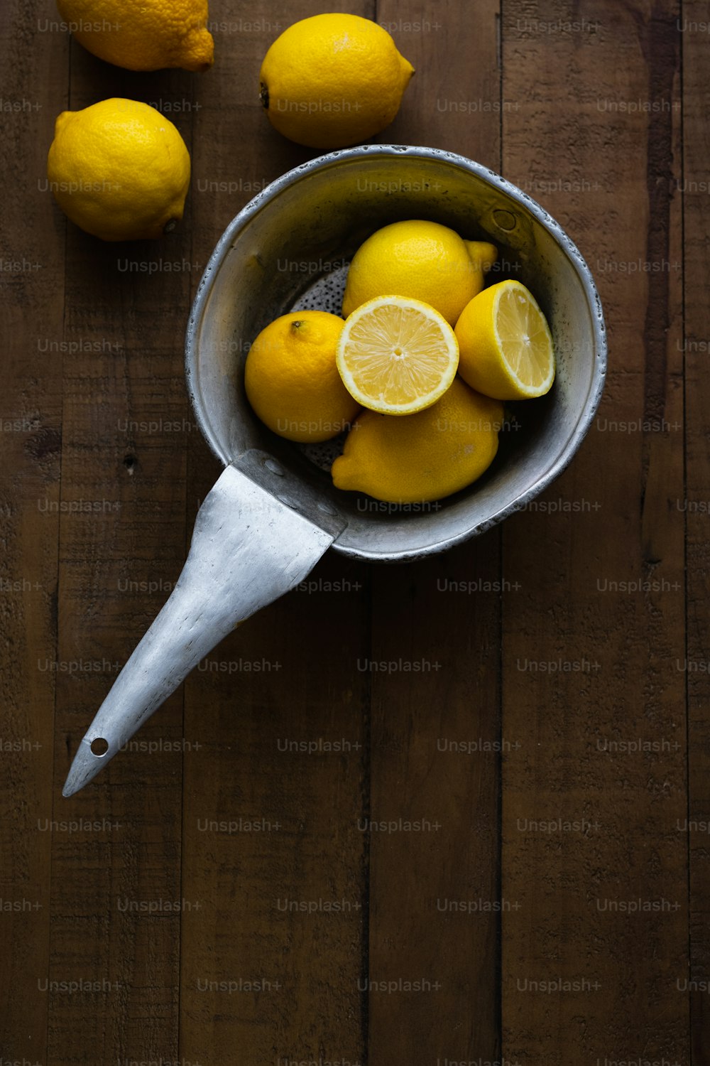 a metal bowl filled with lemons on top of a wooden table