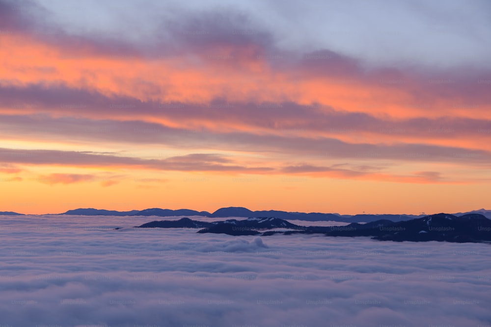 the sun is setting over the mountains above the clouds