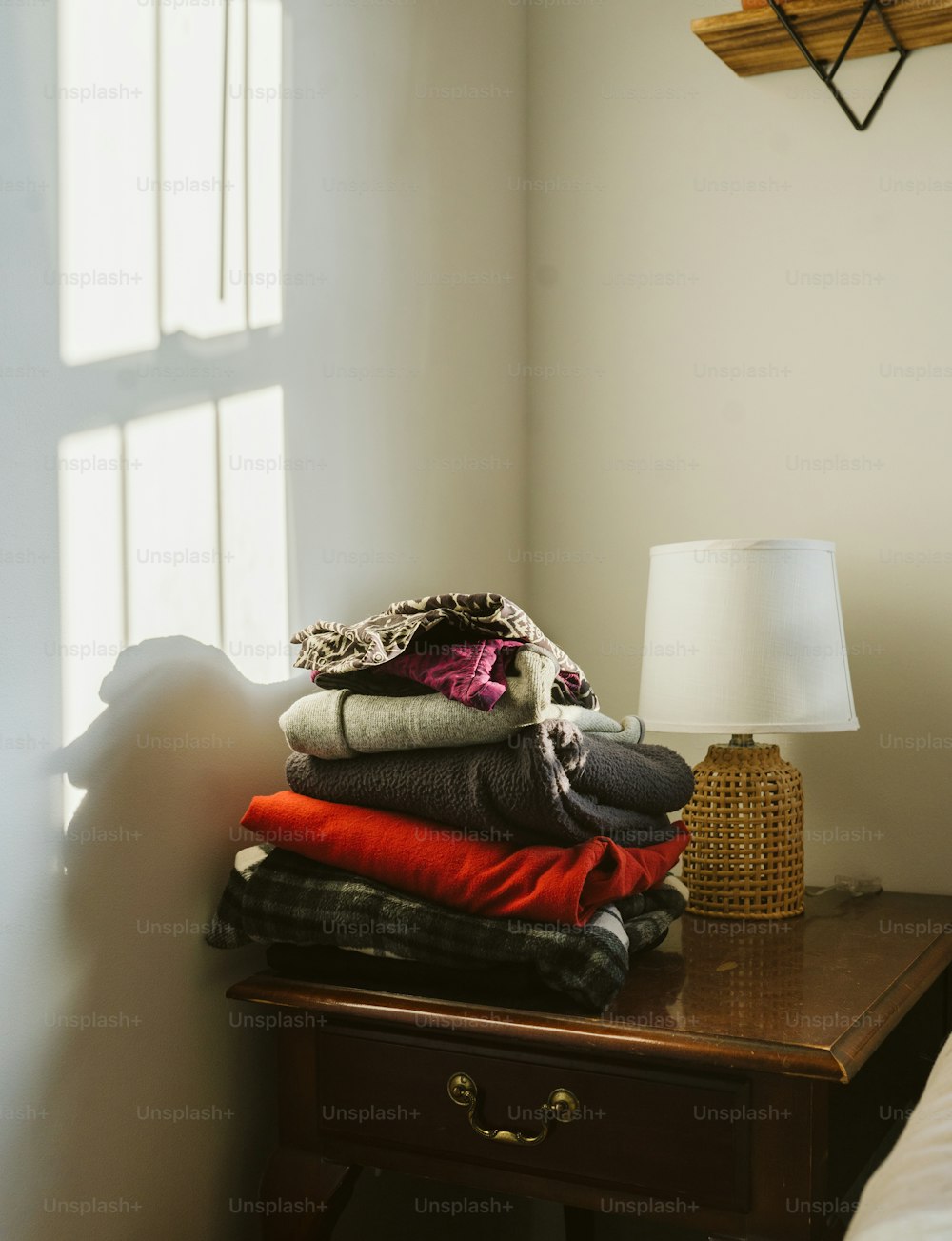 a stack of folded clothes on a table next to a lamp