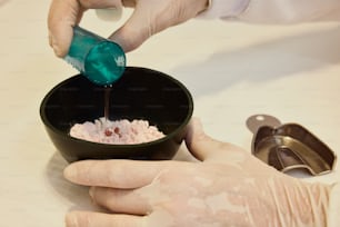 a person in white gloves pouring something into a bowl