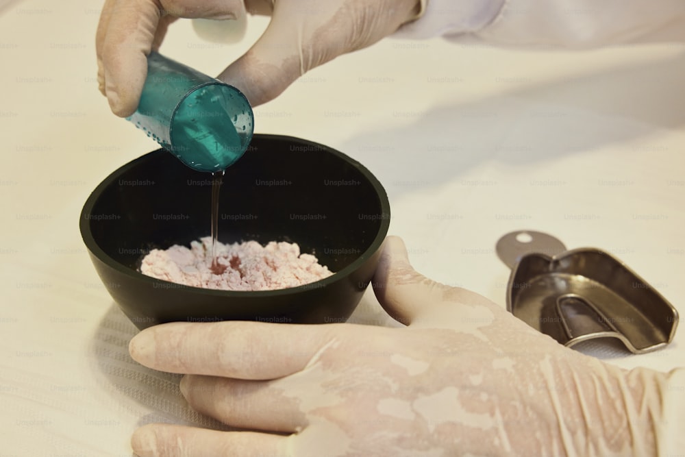 a person in white gloves pouring something into a bowl