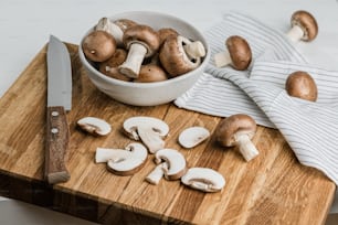 a bowl of mushrooms and a knife on a cutting board