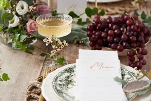 a place setting with a menu, grapes and a glass of wine