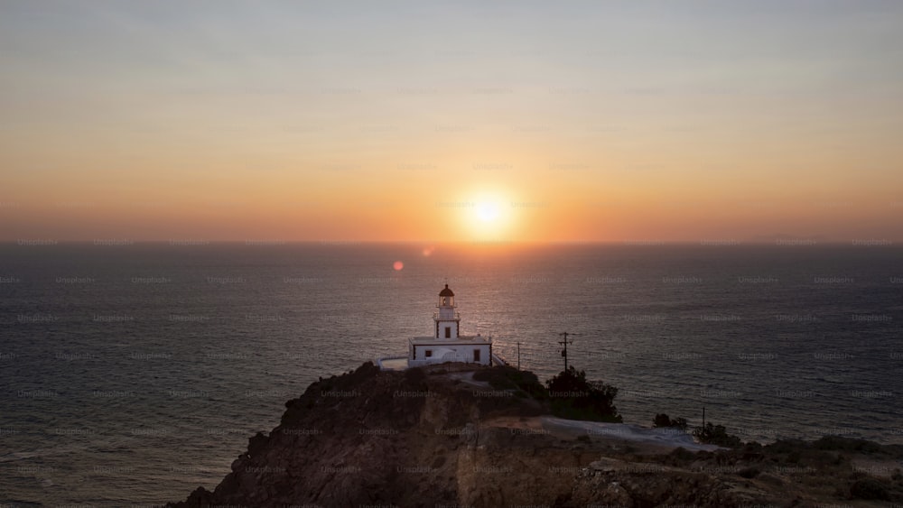 the sun is setting over a lighthouse on a cliff