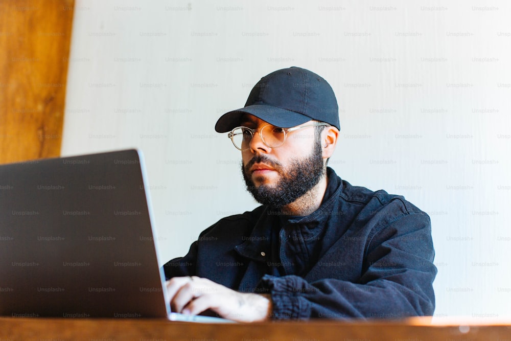 모자와 안경을 쓴 남��자가 노트북을 사용하고 있다