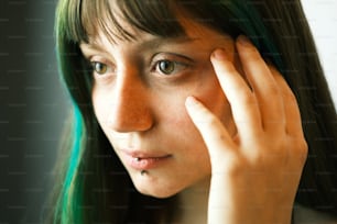 Una mujer con cabello verde sosteniendo su mano hacia su cara