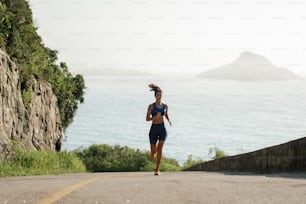 a woman running down a road next to the ocean