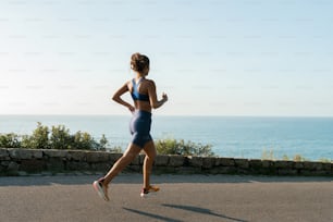 a woman running down a road next to the ocean