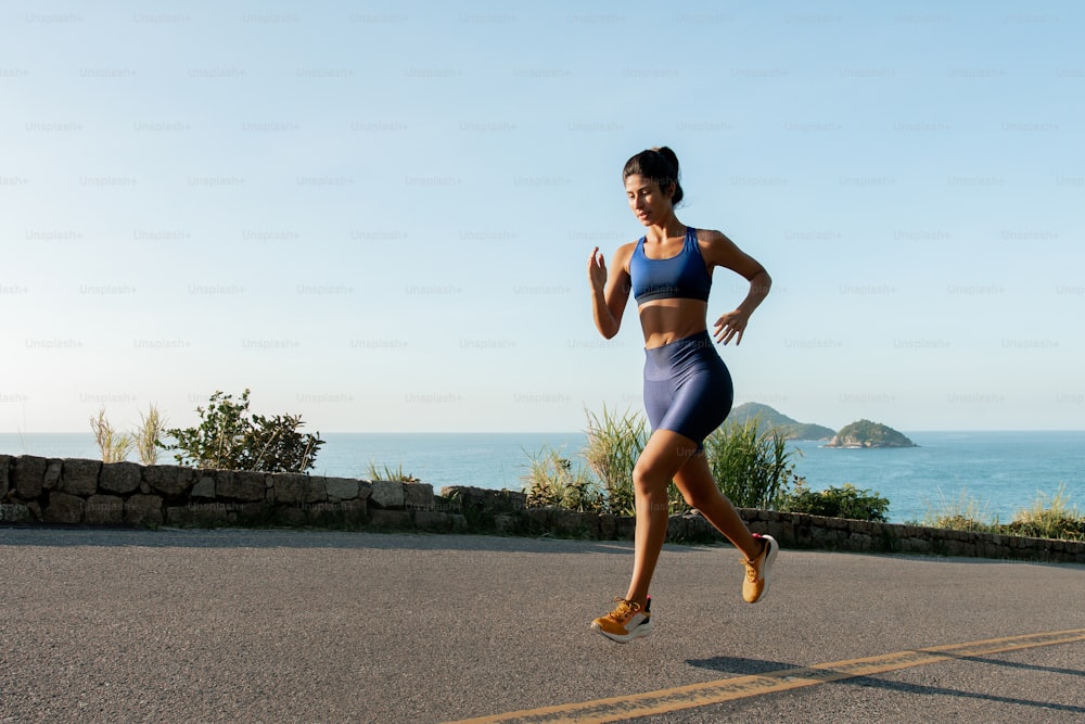 a woman running down a road next to the ocean