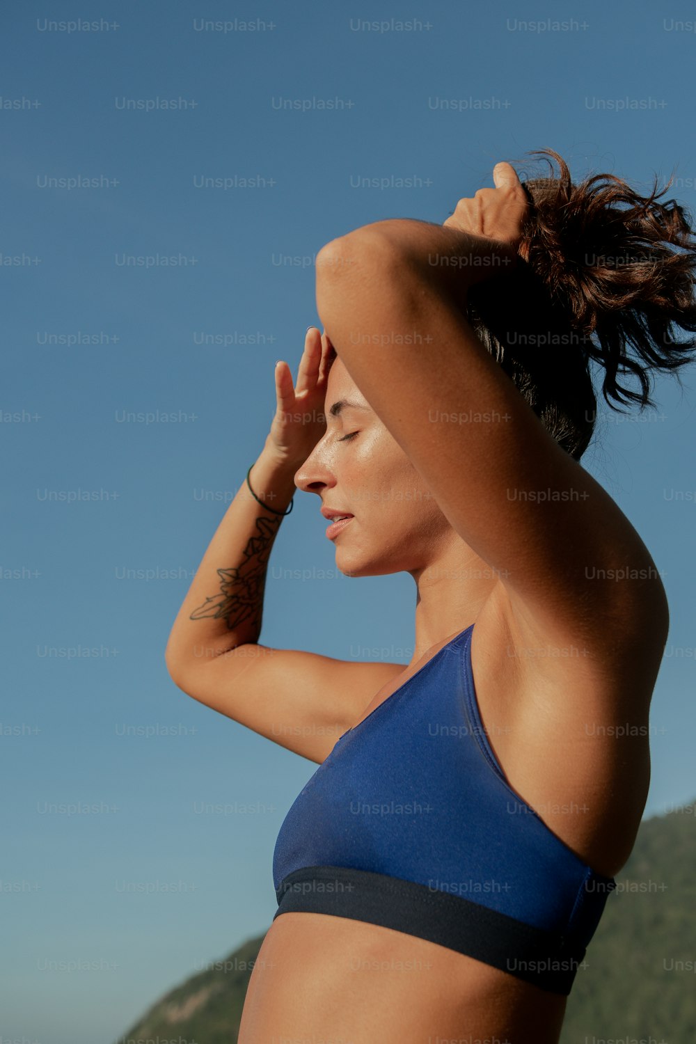 Eine Frau im blauen Bikinioberteil hält ihre Haare