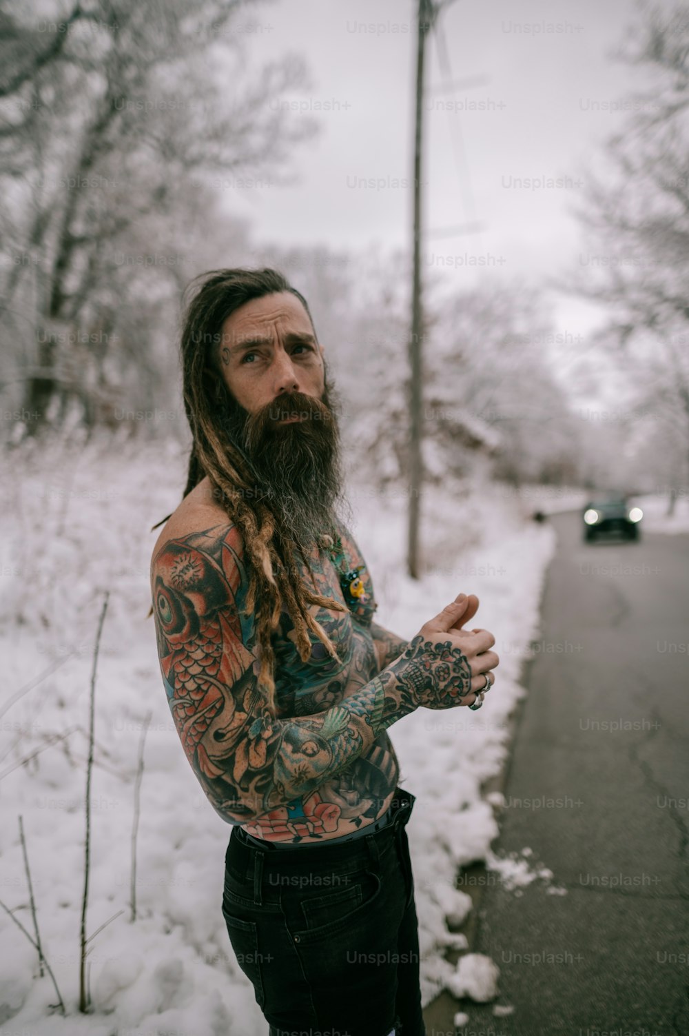 a man with long hair and tattoos standing in the snow
