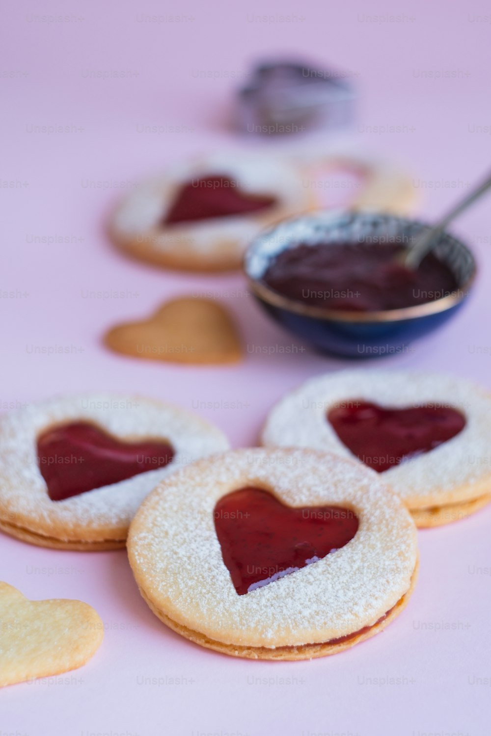 uma mesa coberta com biscoitos em forma de coração ao lado de uma tigela de geleia
