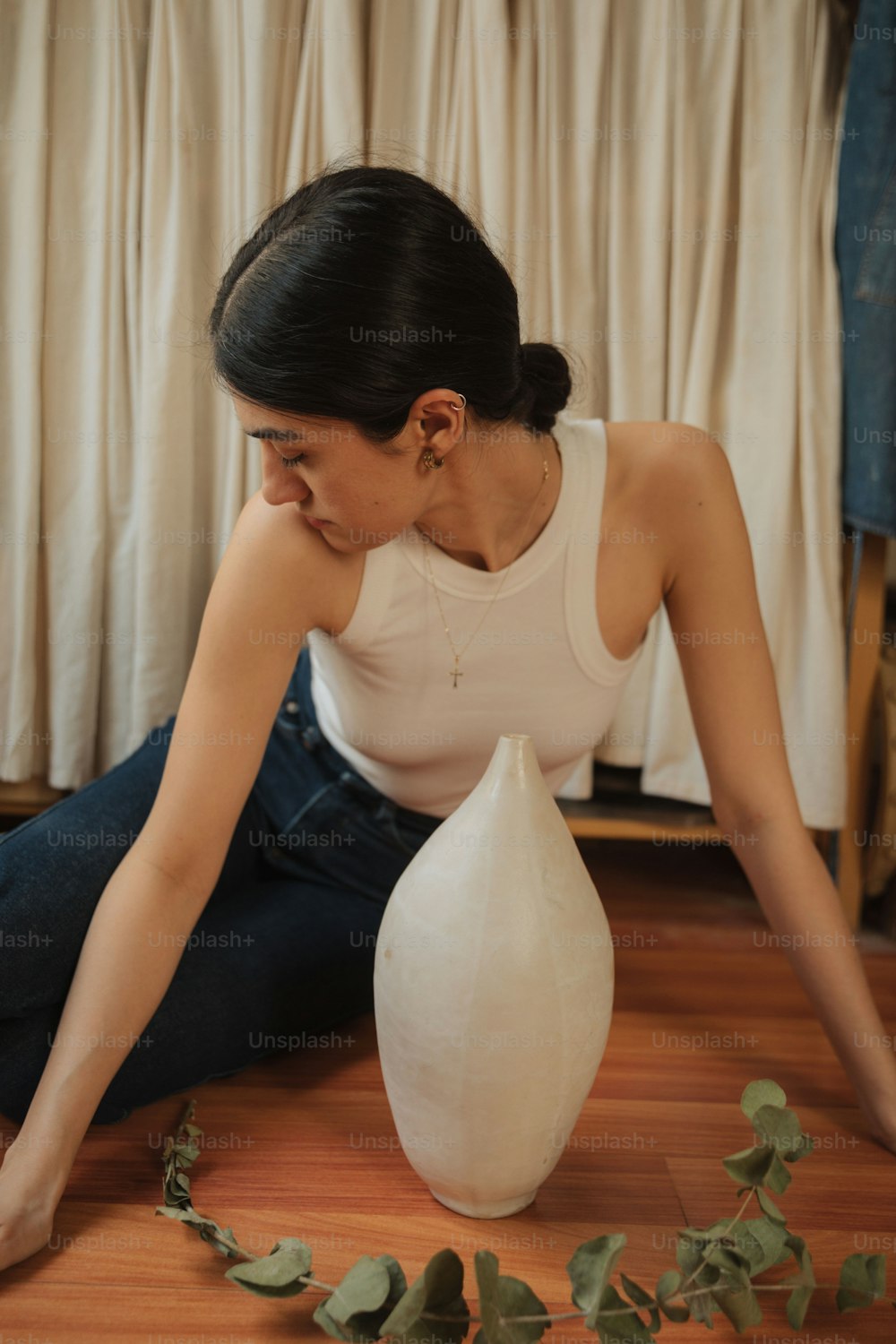 a woman sitting on the floor next to a vase