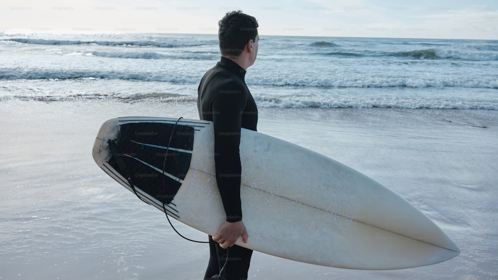 Un hombre con un traje de neopreno sosteniendo una tabla de surf
