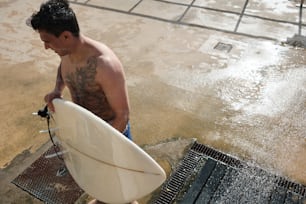 a man holding a white surfboard on top of a wet ground