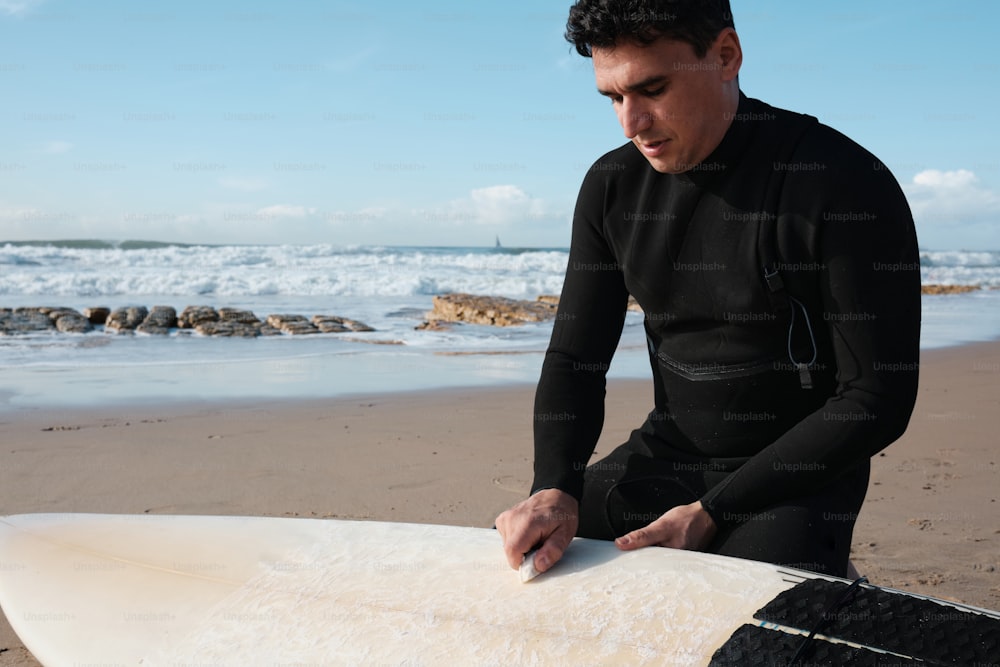Un homme assis sur une plage à côté d’une planche de surf