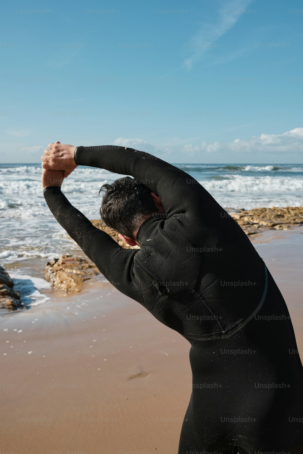 Un hombre con traje de neopreno parado en una playa