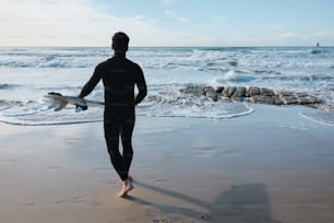 Un homme en combinaison de plongée tenant une planche de surf sur la plage