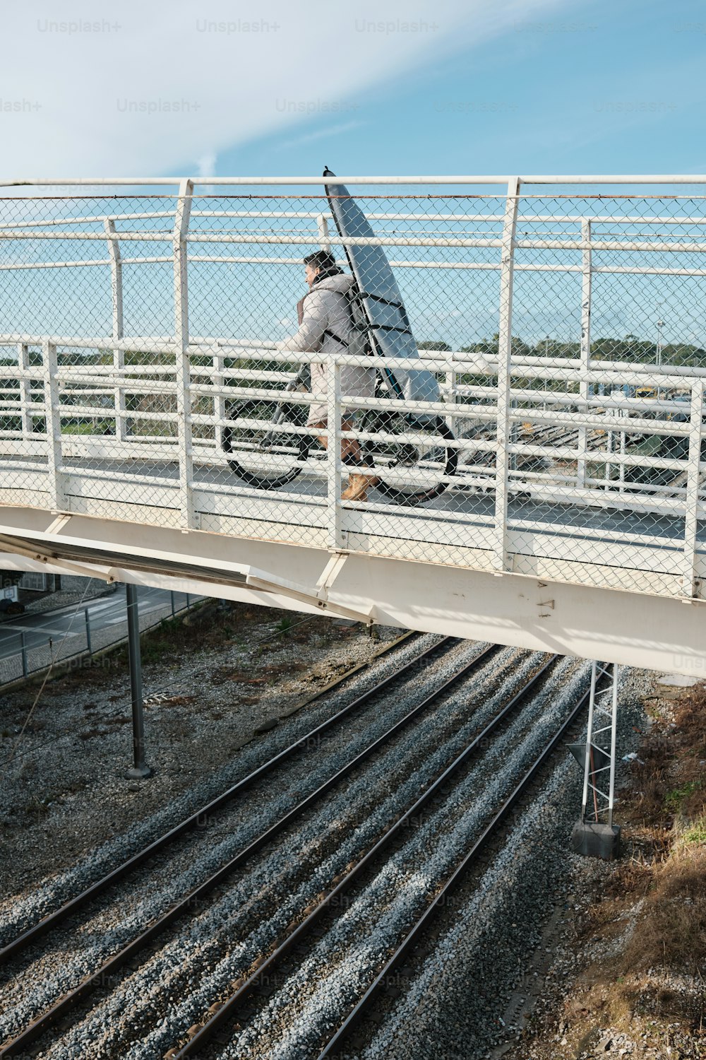 a man walking across a bridge carrying a surfboard