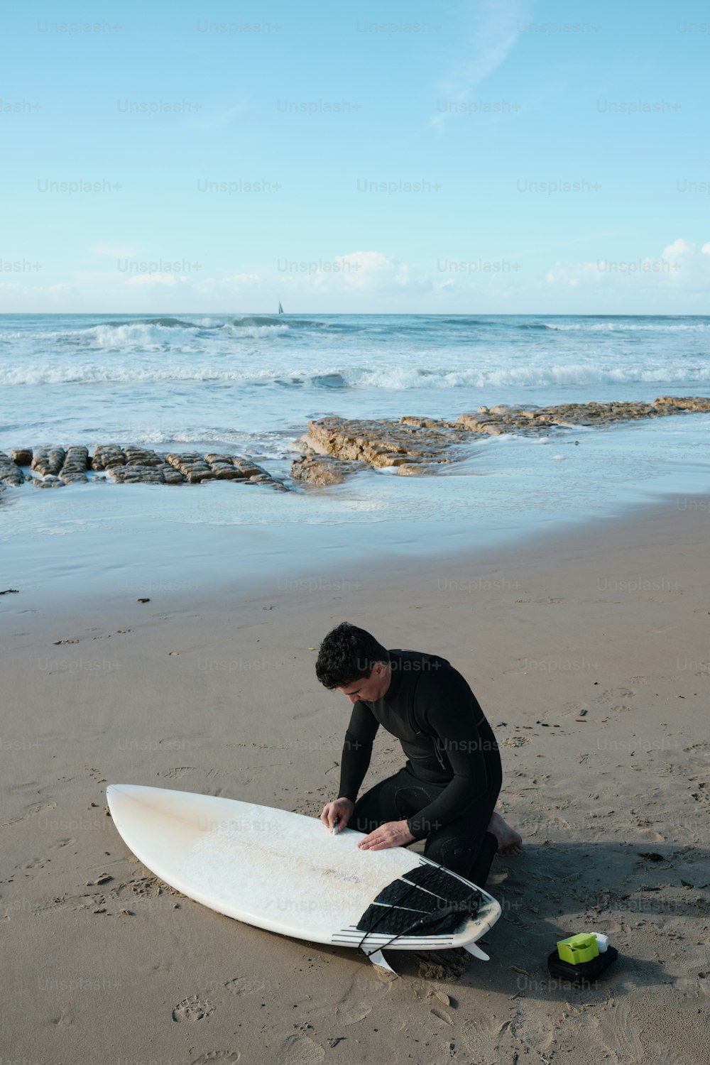 a man sitting on a beach next to a surfboard