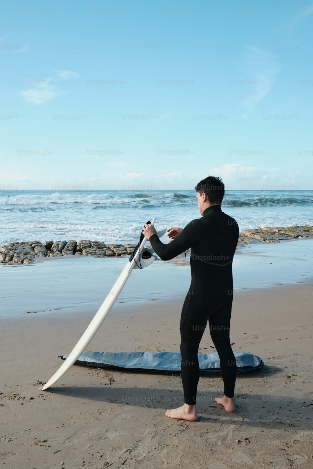 a man in a wet suit holding a surfboard on the beach