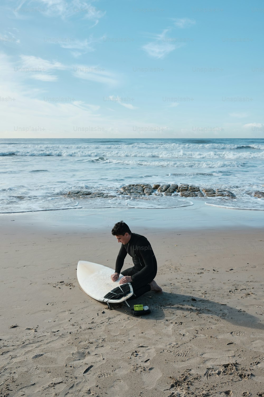 um homem sentado na praia com uma prancha de surf