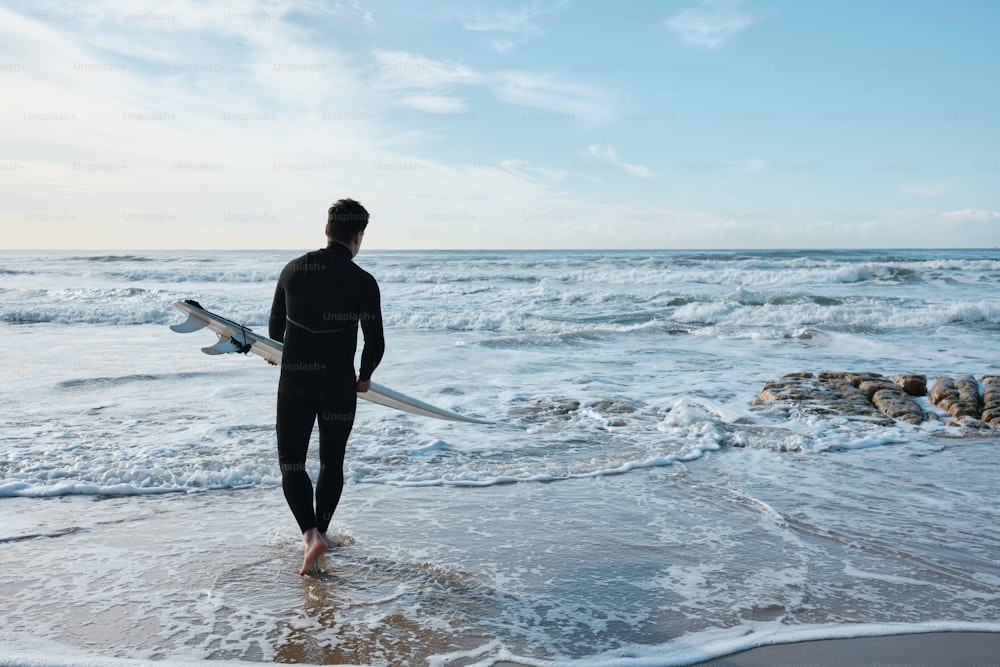 um homem segurando uma prancha de surf andando no oceano
