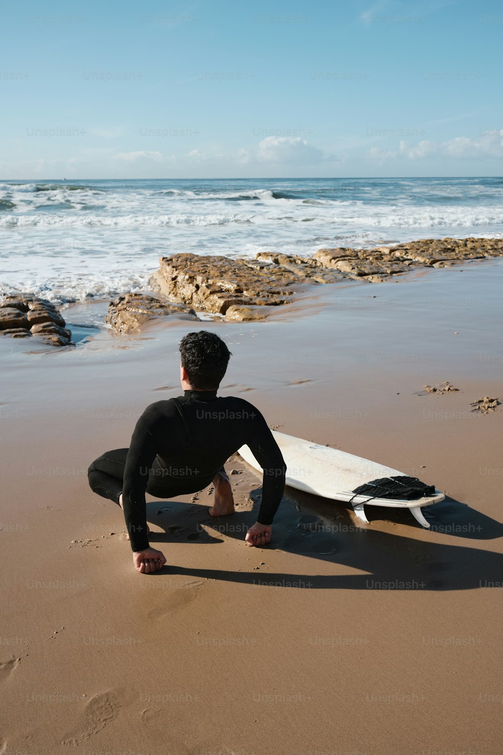 um homem sentado em uma praia ao lado de uma prancha de surf