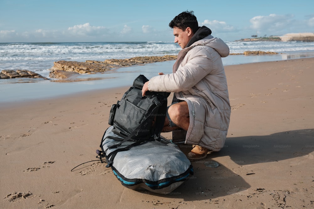 um homem sentado na praia com uma mochila