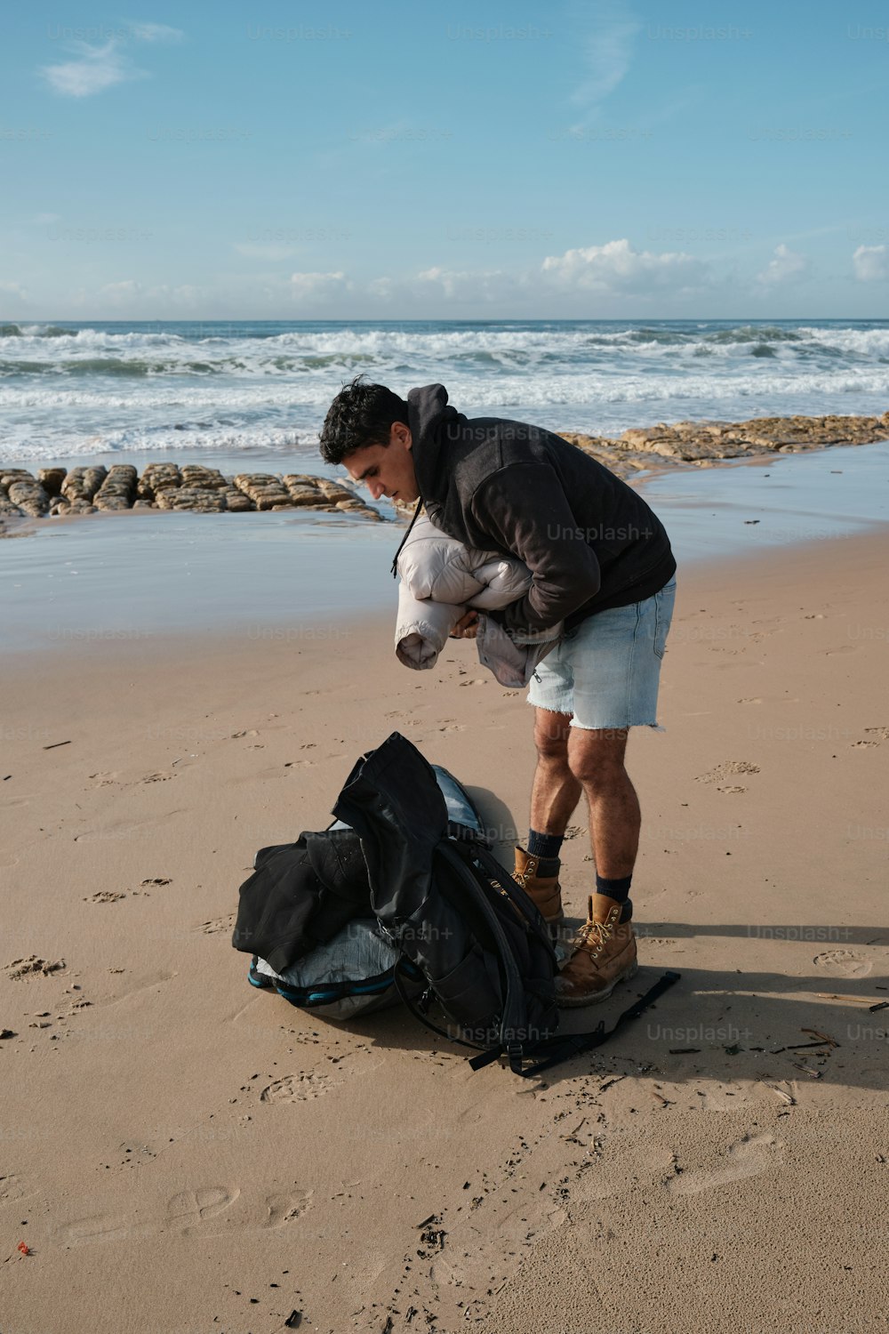 um homem em pé em uma praia ao lado de um saco