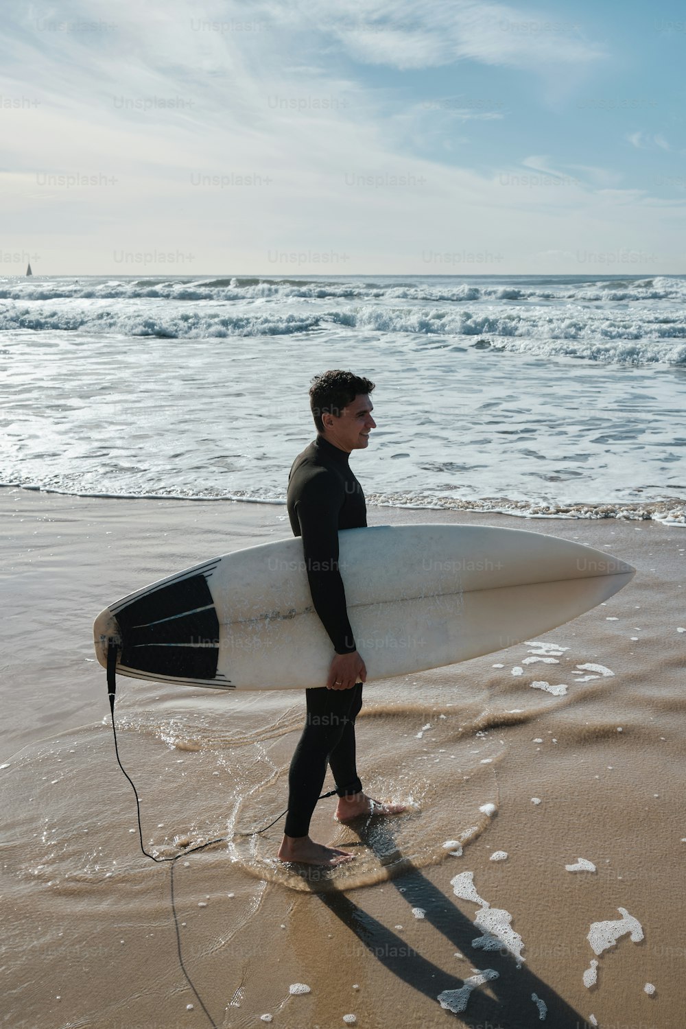 um homem em um traje de mergulho carregando uma prancha de surf na praia