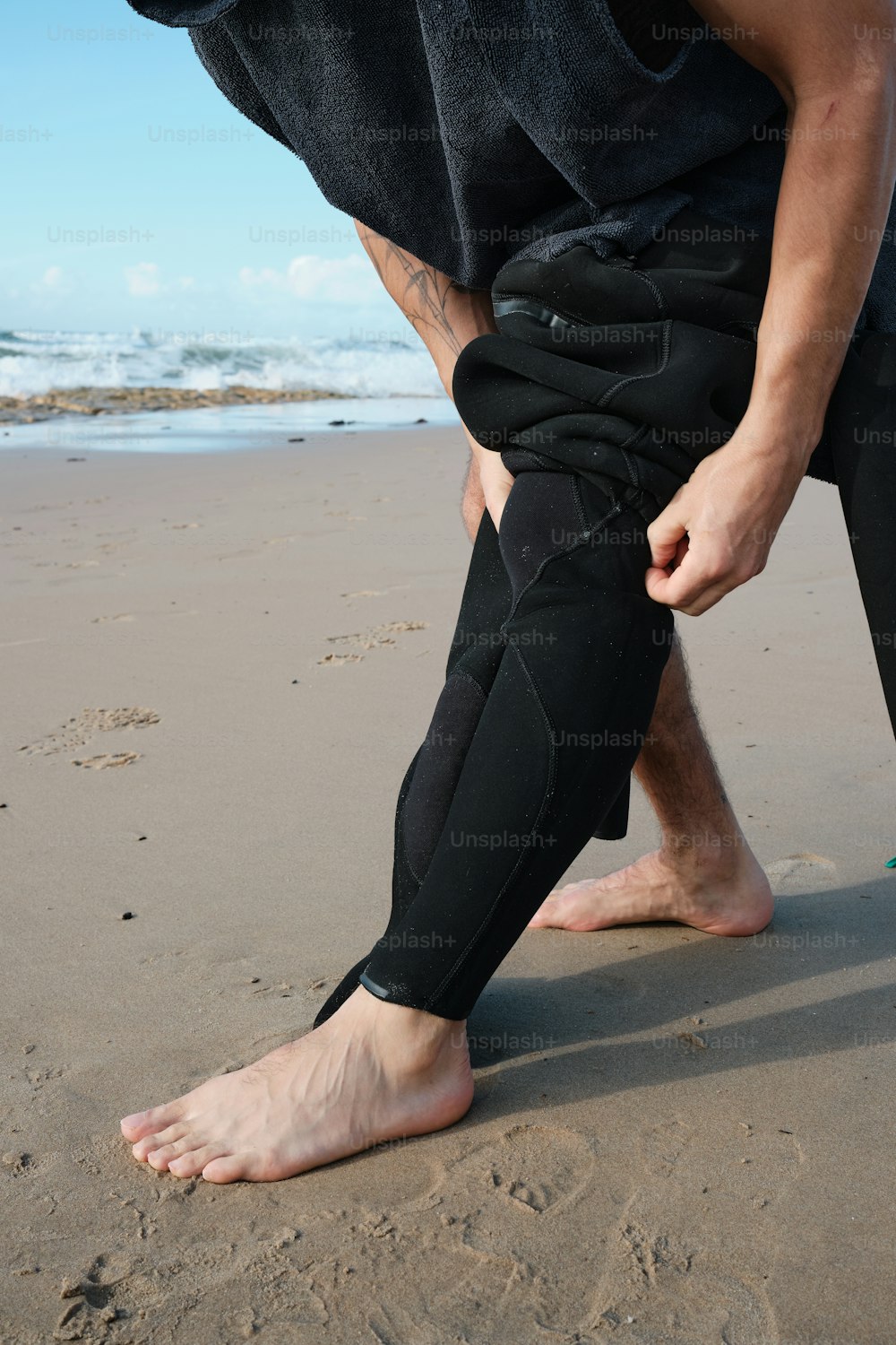 Un hombre con traje de neopreno está parado en la playa