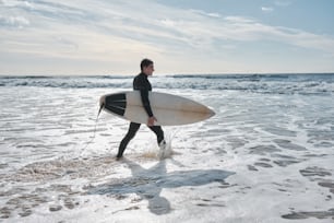 Un hombre con traje de neopreno cargando una tabla de surf en el océano