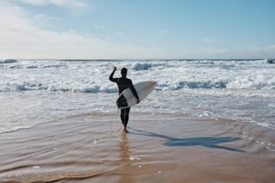 Un homme tenant une planche de surf au sommet d’une plage de sable