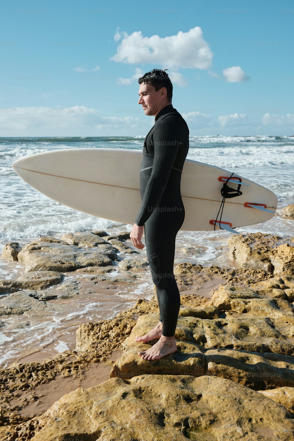 Un hombre con un traje de neopreno sosteniendo una tabla de surf