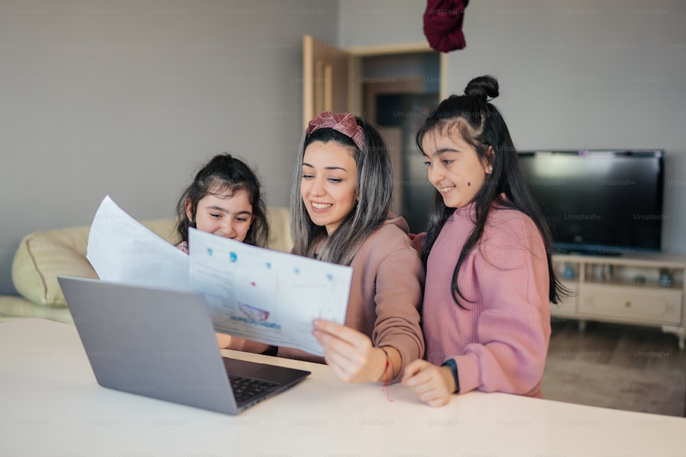 Drei Mädchen schauen auf ein Blatt Papier auf einem Laptop