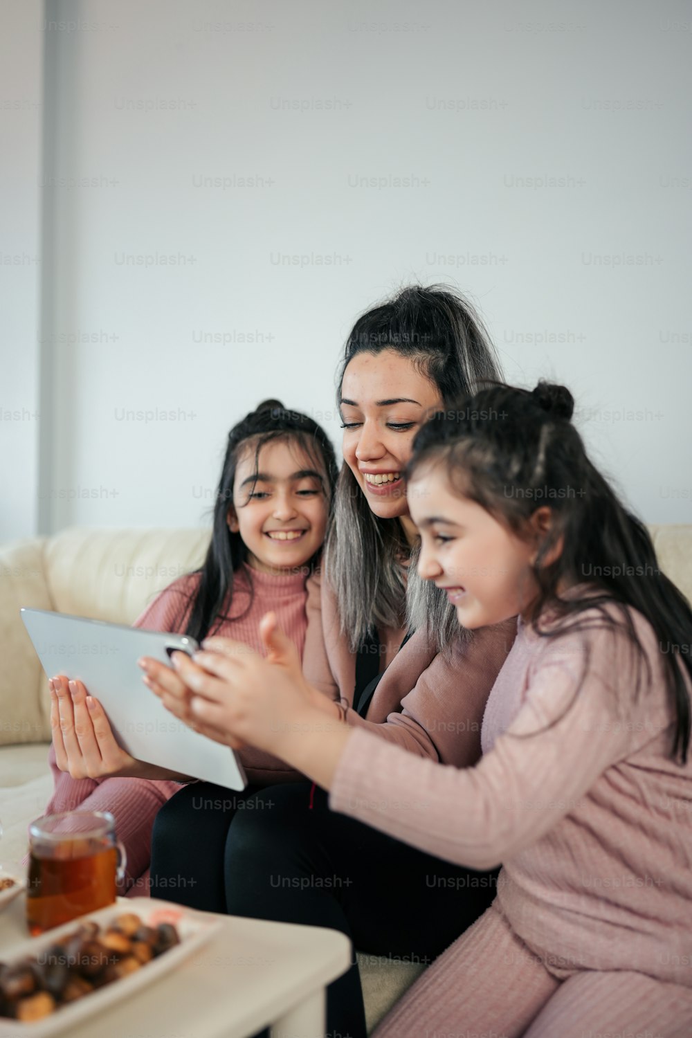 Eine Frau und zwei Mädchen sitzen auf einer Couch und schauen auf ein Tablet