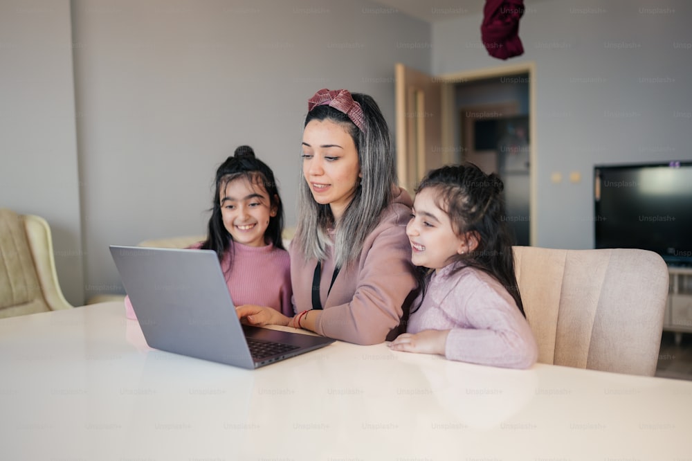 Eine Frau und zwei Mädchen sitzen an einem Tisch und schauen auf einen Laptop