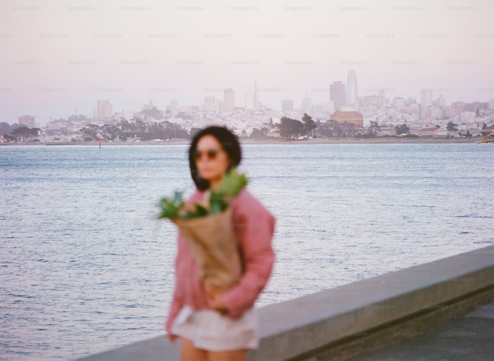 a woman holding a bouquet of flowers near a body of water